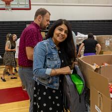 Volunteer standing in front of boxes filled with supplies as they pack backpacks