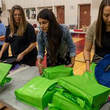 Volunteers standing at tables with school supplies as they pack them into backpacks