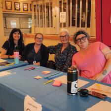 Four females sitting at a registration table waiting to welcome participants